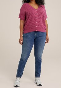 Rosa kortärmad tröja med V-hals och diagonalt ribbat mönster, kombinerad med blå slim-fit denimjeans och vita sportskor.