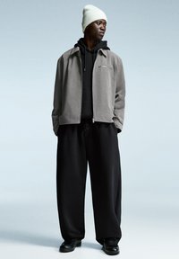 Gray jacket over a black hoodie, paired with black wide-leg pants and black shoes. The individual wears a white knit beanie.
