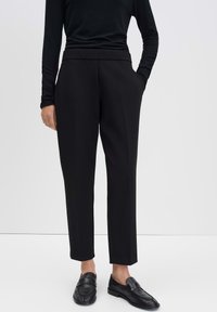 Zwarte op maat gemaakte broeken met een hoge taille, rechte snit en zijzakken. Gemaakt in combinatie met een zwart langemouwen top en zwarte schoenen.