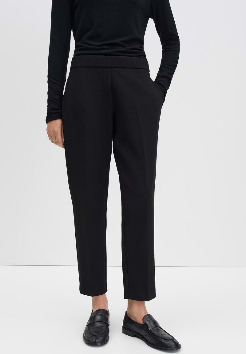 Zwarte op maat gemaakte broeken met een hoge taille, rechte snit en zijzakken. Gemaakt in combinatie met een zwart langemouwen top en zwarte schoenen.