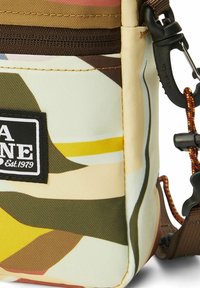 Piccola borsa a tracolla con motivo astratto multicolore, cerniera nera, patch con logo e clip in plastica nera attaccata con cordino marrone.
