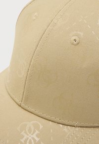 Casquette de baseball beige en tissu texturé, avec un motif en relief et des coutures visibles. Comprend un œillet de ventilation rond.