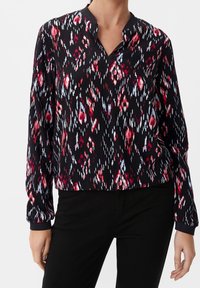 Blusa de manga larga en negro con un patrón abstracto en rojo y azul, con escote en V y puños elásticos, fabricada con un tejido ligero.