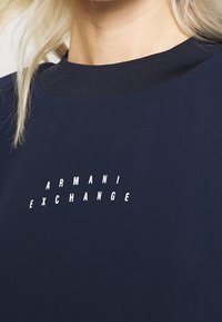 Marinblå sweatshirt med ribbat rundhals, med vit "ARMANI EXCHANGE" text över bröstet. Slät tygkvalitet.