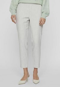Pantalons taillés gris clair en tissu lisse et texturé. Design slim-fit avec taille mi-haute et jambes effilées, agrémenté de plis avant.