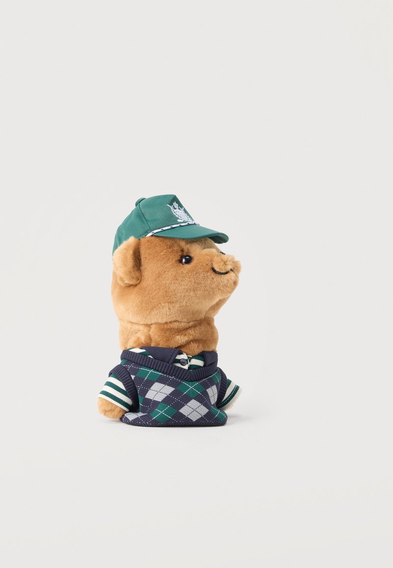 Πελώριο παιχνίδι σκύλου που φοράει πράσινο καπέλο και γιλέκο με μοτίβο αργκλάι πράσινης και μπλε απόχρωσης, με ριγέ πουκάμισο από κάτω, στραμμένο προς τα δεξιά σε λευκό φόντο.