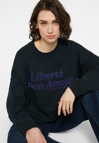 Schwarzer Sweatshirt mit lila Text "Liberté mon Amour." Verfügt über einen Rundhalsausschnitt und einen lockeren Schnitt, mit gerippten Bündchen und Saum.