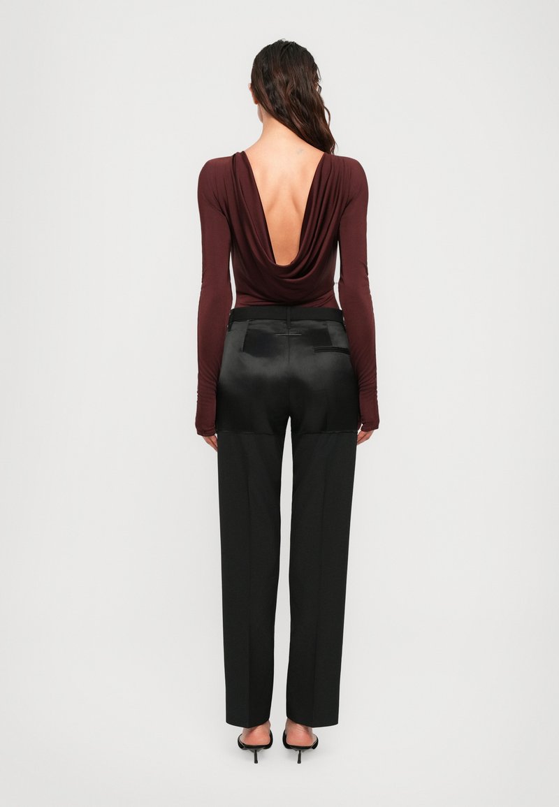 Donna che indossa una maglietta a maniche lunghe di un rosso scuro con schiena aperta profonda, pantaloni neri a vita alta con dettagli in satin e sandali neri con tacco.