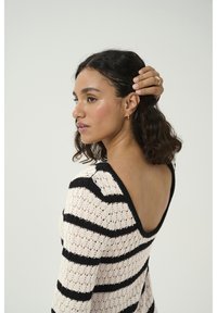 Pull en tricot avec de larges rayures noires et crème, décolleté profond au dos, manches longues et tissu texturé. Met en valeur le design du dos ouvert.