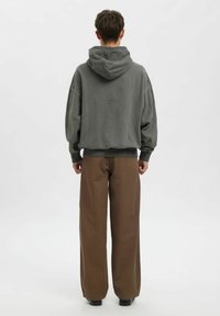 Šedá mikina s kapucí, volného střihu a s žebrovanými manžetami. Kombinována s širokými hnědými kalhotami, oba kousky mají minimální značení a textury.