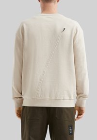 Beige sweatshirt met een diagonale naaddetail op de achterkant. Gemaakt van zachte stof, met ribgebreide manchetten en een afgeronde zoom.