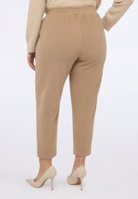 Khaki prążkowane spodnie z elastycznym pasem, zwężanymi nogawkami i gładką teksturą. Połączone z beżowymi szpilkami.