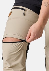 Beige utomhusbyxor med svarta detaljer; har ett zip-funktion vid knäet. Tillverkade av ett slitstarkt, lätt tyg med en mjuk yta.