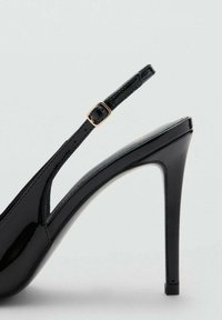 Čierne lakované lodičky na vysokom opätku so špicatou špičkou, štíhlým pásikom a detailom zlatého tónu na členku.