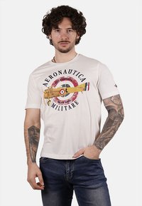 T-shirt bianca in cotone con una grafica di un biplano e un'insignia circolare. Maniche corte e design a colletto rotondo.
