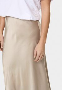 Silkkinen midimallinen hame beige sävyssä, jossa on sileä rakenne ja hillitty kiilto. Yhdistettynä löysään valkoiseen t-paitaan, mikä luo rentoa tyyliä.