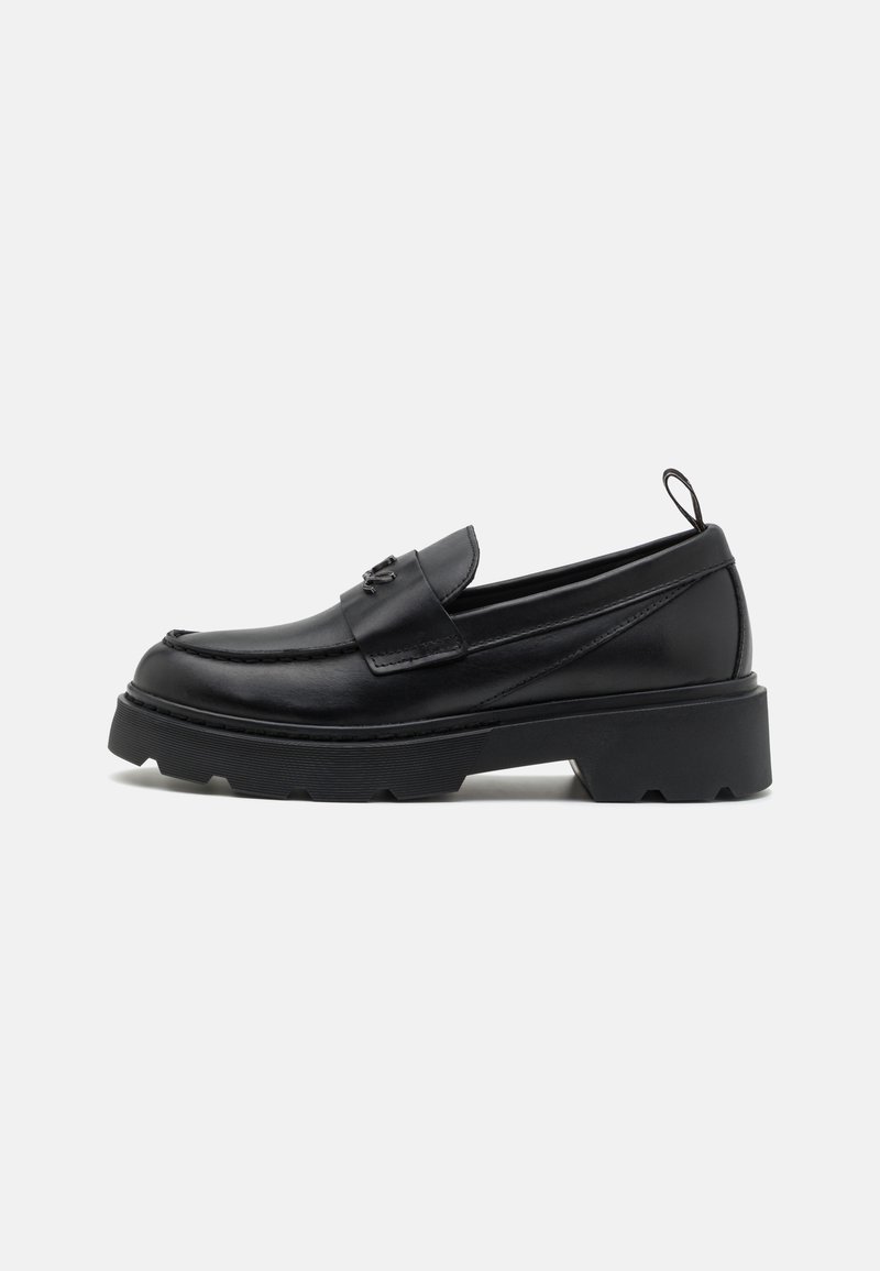 Sapatos loafers de couro preto com bico arredondado, sola plataforma robusta e uma tira decorativa na parte frontal. Detalhes texturizados na parte superior.