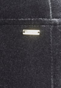 Black fabric with a soft texture features a visible seam and a small gold "TASCA" label attached. The design is simple and minimalistic.