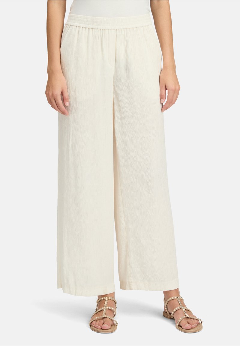 Pantalon ample à jambes larges de couleur crème avec un tissu texturé et une taille élastique, associé à des sandales plates ornées de perles.