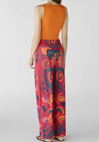 Débardeur orange à côtes associé à un pantalon large arborant un motif floral et feuillu vibrant dans des tons de rose, vert et orange.