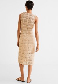 Robe en dentelle beige avec motif ondulé, design sans manches et ourlet jusqu'aux genoux. Dos équipé d'une fermeture éclair invisible. Tissu texturé.