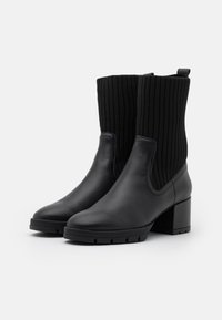 Mustat nilkkurit, joissa on sileä nahkainen kärki ja kanta, varustettuna ribatulla neulepäälliosalla ja paksulla lohkokannalla. Teksturoitu musta materiaali.