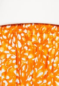 Elastisk midja med samlad detalj, med ett djärvt orange och vitt abstrakt mönster på lätt tyg.