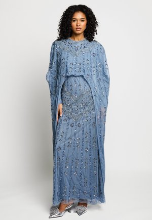 Mujer con cabello rizado que lleva un vestido azul hasta el suelo con elaborados bordados de cuentas y lentejuelas, combinado con tacones adornados en plata.