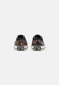 Sneakers neri in tela con un design leopardato sul tallone, suola in gomma beige e marchio "Converse All Star" in nero sul retro.
