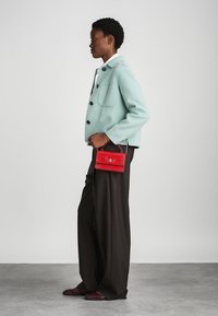 Mintgrüne Jacke mit schwarzen Knöpfen, kombiniert mit weiten braunen Hosen und einer kleinen roten Tasche im Krokodil-Design mit einem silbernen Kettenriemen.