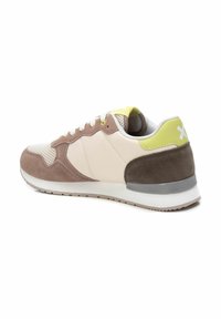 Zapatillas deportivas con parte superior de malla en beige claro, detalles en ante marrón y un tirador en neón amarillo en el talón. Suela de goma con borde gris.