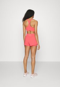 Rosa sport-BH med racerback-design och matchande lättviktsshorts. Texturen är slät, idealisk för aktiva kläder. Sportskor i ljus rosa.