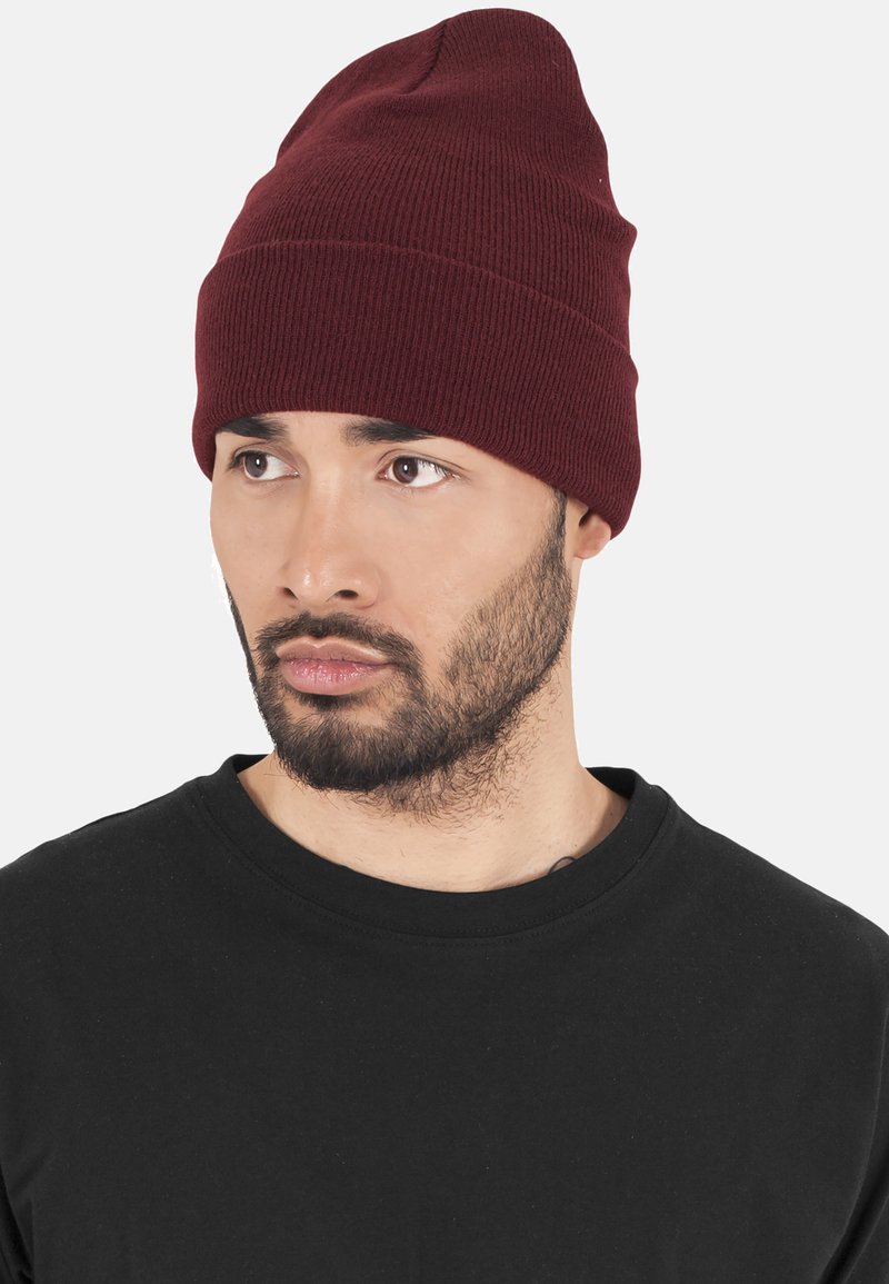 Knit beanie in burgundy, soft texture, ribbed design, tapering shape, worn slightly slouched, paired with a black crew-neck t-shirt.