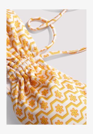 Geel en oranje bloemenprintstof met geplooide stiksels en dunne bandjes op een lichte achtergrond.