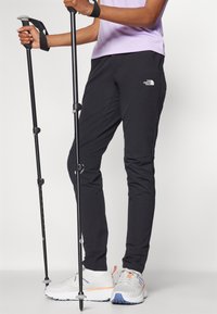 Černé turistické kalhoty z odolné, pružné tkaniny s úzkým střihem. Mají boční kapsy a logo na levém boku.