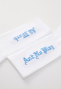 Hvite ribbede sokker med blå broderte tekst, som leser "prome" og "Don't No Play," plassert ved siden av hverandre. Mykt materiale, uformell design.