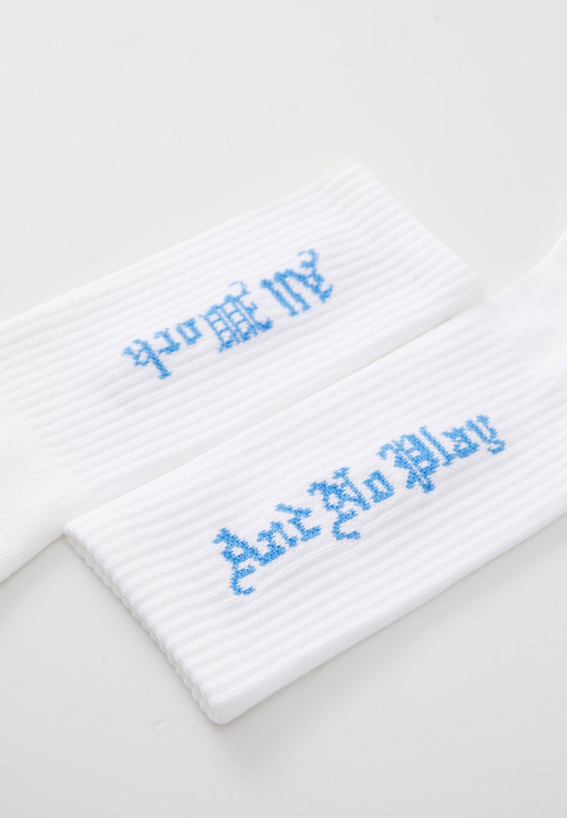 Witte geribde sokken met blauwe geborduurde tekst, leesend "prome" en "Don't No Play," zij aan zij gepositioneerd. Zacht materiaal, casual ontwerp.