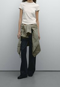 Witte, getailleerde t-shirt in combinatie met wijde marineblauwe broek en een olijfgroene jas geknoopt om de taille. Glad materiaal, casual ontwerp.