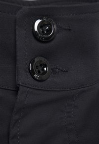 Black fabric waistband featuring two glossy buttons with engraved logos. The surface is smooth with visible stitching details.