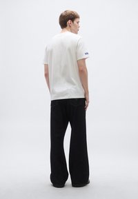 Bela bombažna majica s kratkimi rokavi, z modrim logotipom na levi rokavi. Kombinirana z ohlapnimi črnimi kavbojkami.