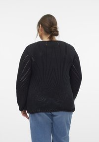 Mustat neulotut neuleet, joissa on tekstuurinen, avoneuloskuvio ja kukkakoristeet. Pitkät hihat ja mukava istuvuus, yhdistettynä sinisiin farkkuihin.