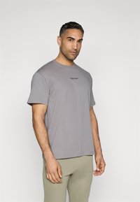 Tricou din bumbac gri, cu mâneci scurte, guler rotund și o marcaj subtil pe piept. Textură netedă cu o croială lejeră.