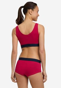 Red cotton sports bra with a navy band, paired with red hipster shorts featuring a navy waistband. Smooth texture, simple design.