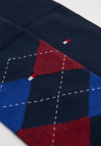 Marineblaue Socken mit einem geometrischen Muster aus roten und blauen Rauten sowie weißen Akzenten, gefertigt aus einem strukturierten Strickmaterial.