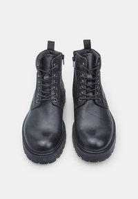 Stivali in pelle nera con punta rotonda, chiusura con lacci, cerniere laterali e parte superiore testurizzata con cuciture rinforzate. Suola in gomma per una buona aderenza.