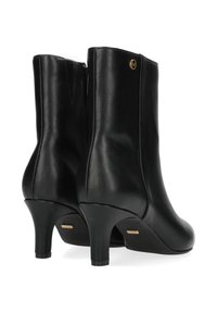 Černé kožené kotníkové boty s hladkým povrchem, zúženými vysokými podpatky, bočním zipem a malým zlatým logem na vnější švu.