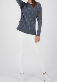 Szara bluza z kropkami, różowymi akcentami i naszywką z logo. W zestawie z białymi, dopasowanymi dżinsami i białymi sneakersami. Czysty, casualowy look.