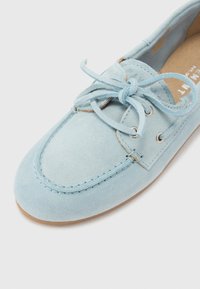 Svijetloplave suede mokasine s zaobljenim prstom, pertlama sprijeda i srebrnim okovima. Sadrže šivane detalje i smeđu gumenu potplatu.