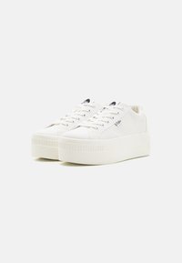 Vita kanvas sneakers med en tjock, strukturerad sula, rund tå och platta snören. Har en liten logotyp på sidan och en subtil bakre detalj.