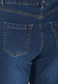 Pantalones vaqueros de mezclilla en azul oscuro con una textura suave, que presentan un bolsillo trasero con una costura en contraste de color marrón claro y un diseño ajustado.